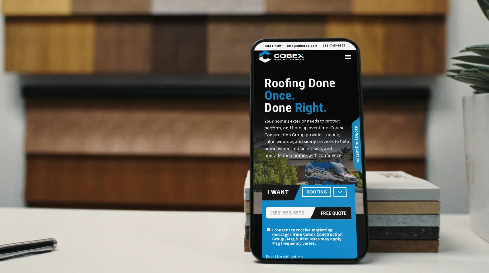 The Cobex Construction Group website on a phone on a roofing showroom counter with sample boards