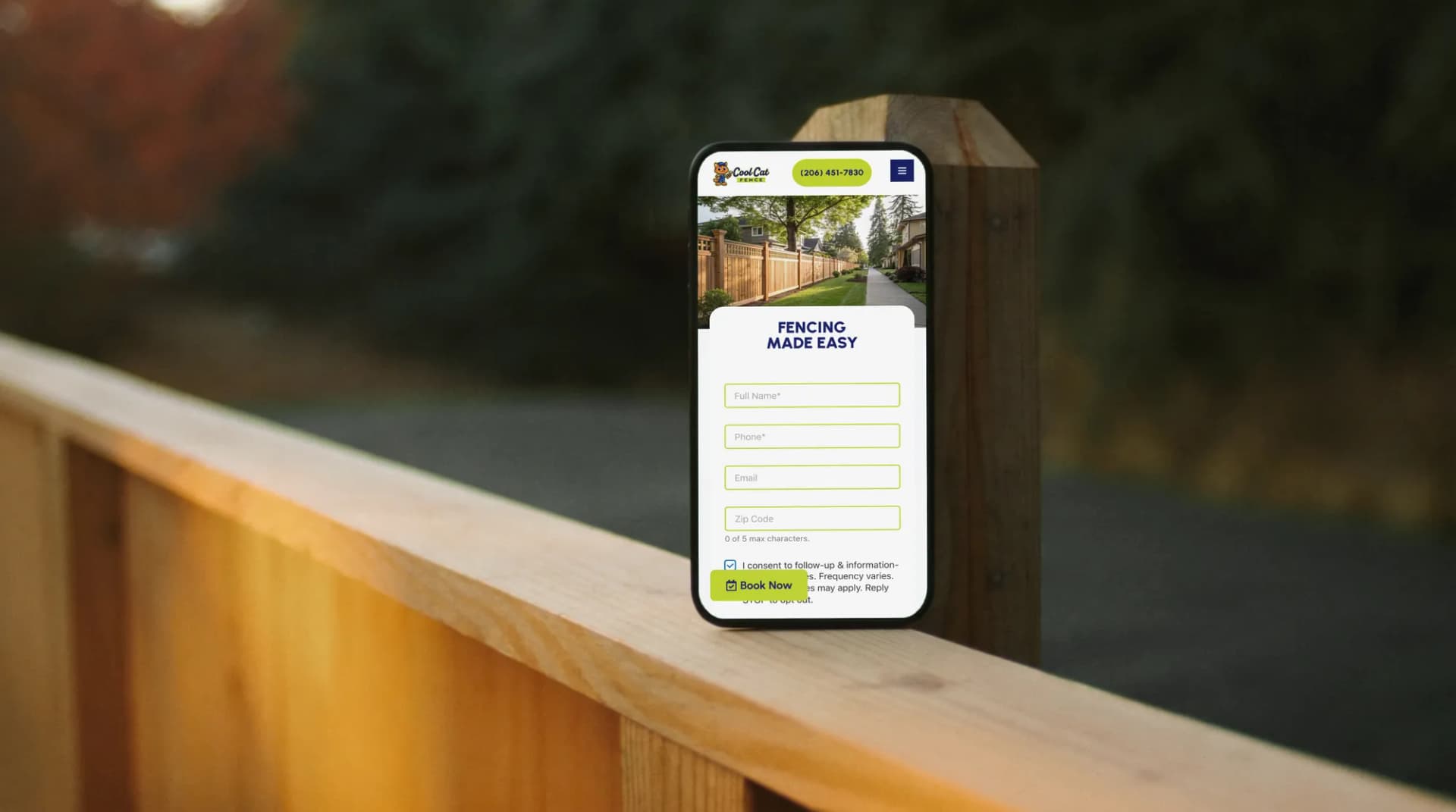 The Cool Cat Fence website on a phone on the top rail of a new cedar fence at golden hour