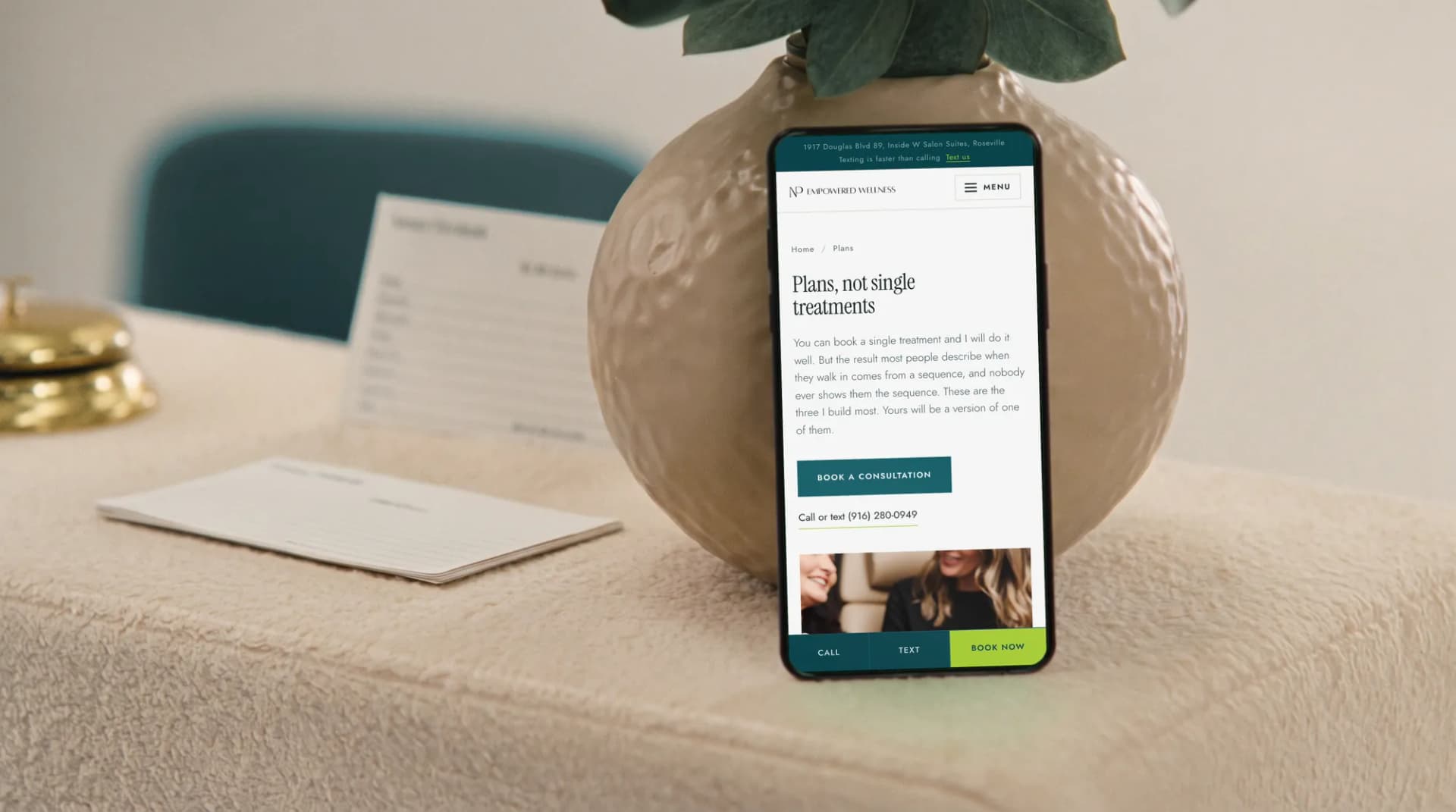 The NP Empowered Wellness plans page on a phone on a clinic reception desk beside eucalyptus