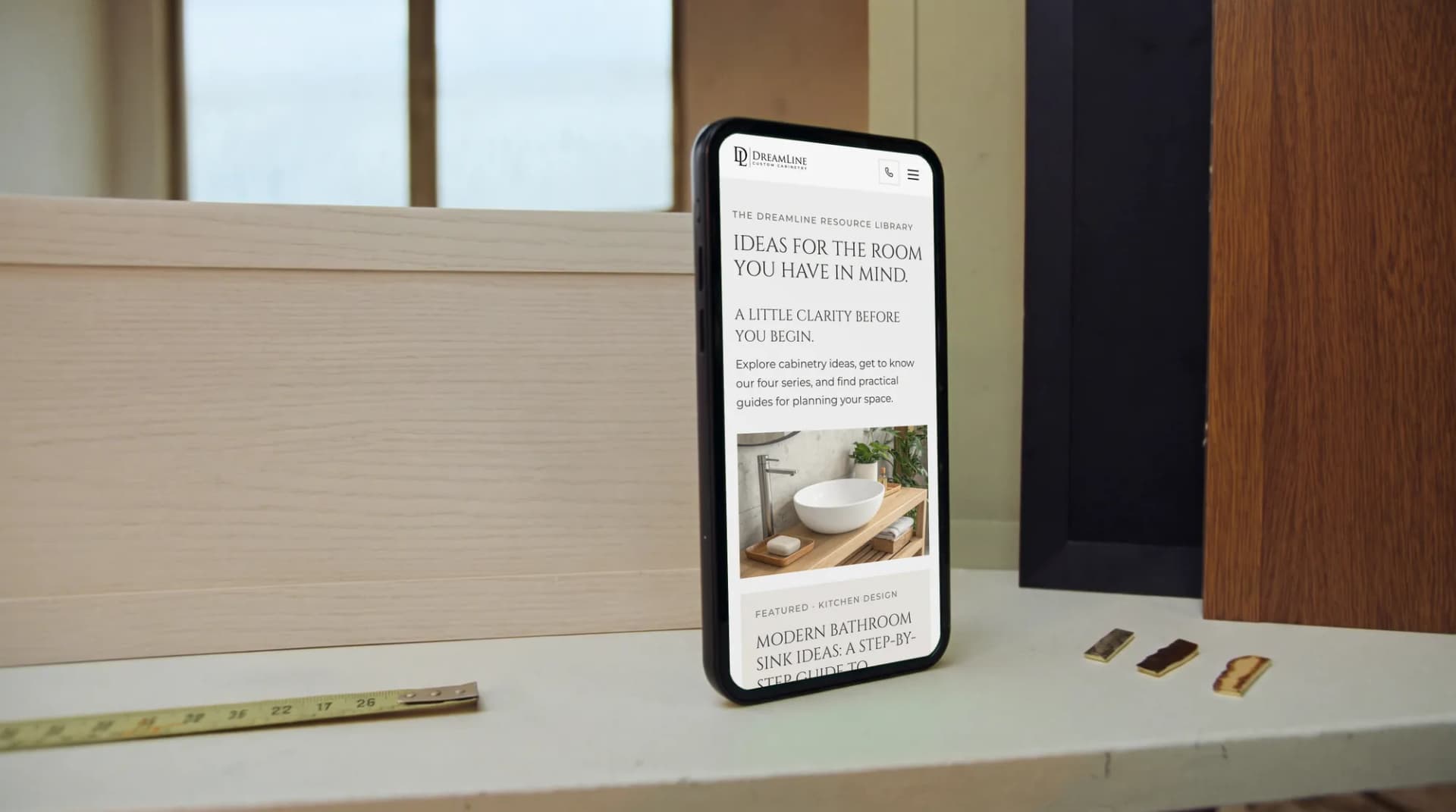 The Dreamline Cabinetry resource library on a phone beside cabinet-door samples on an oak table